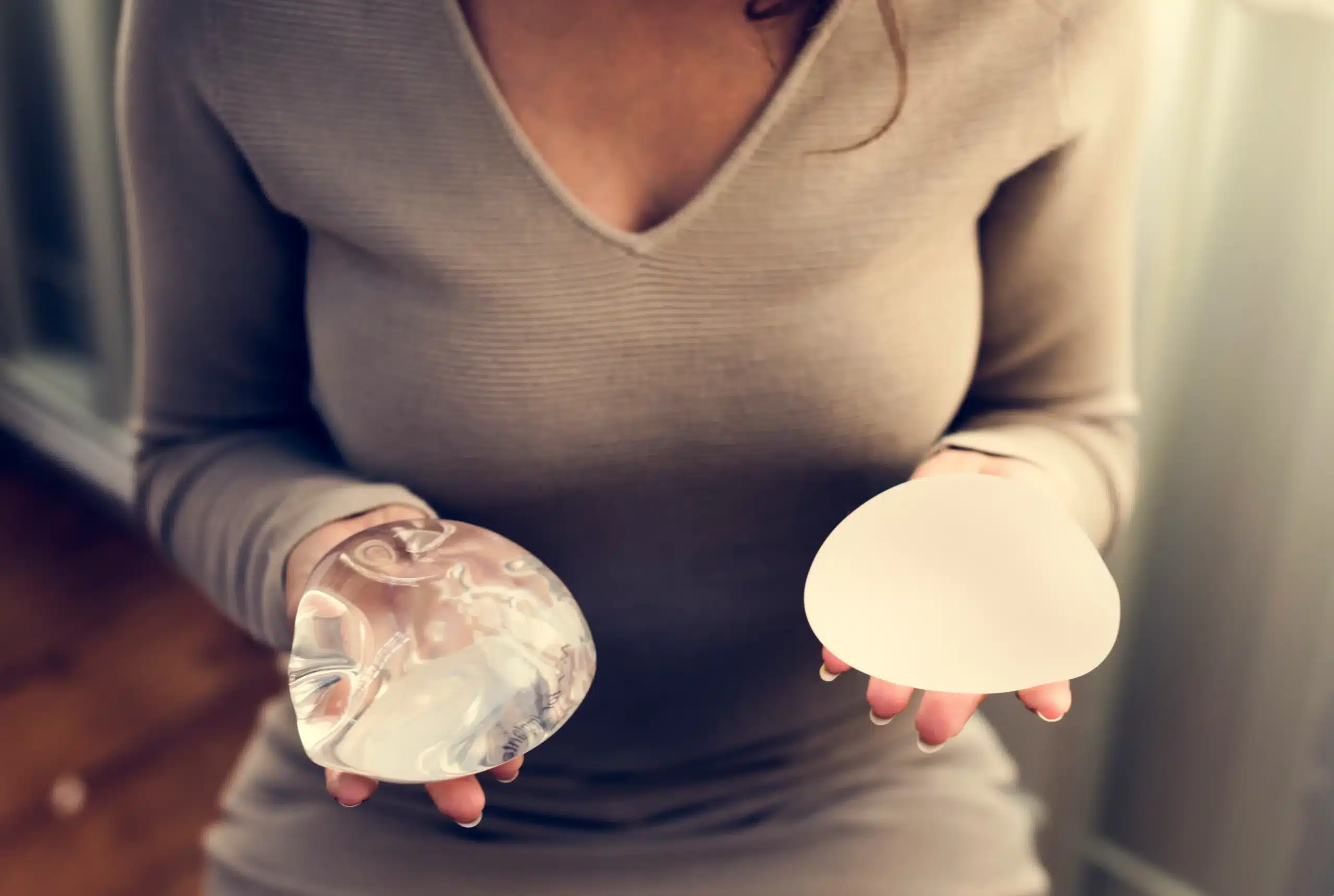 Woman holding a saline and a silicone breast implant, comparing the two types side by side